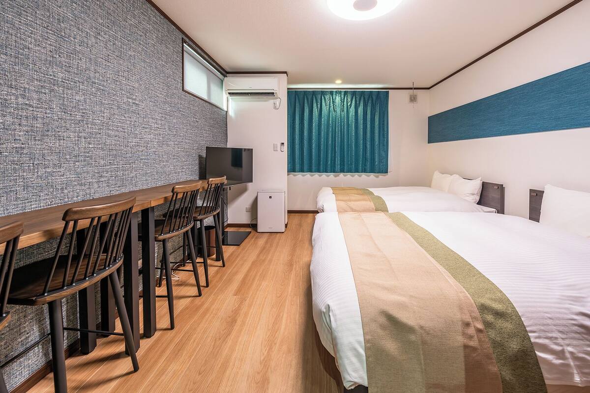 A hotel room with a wooden desk, chairs, a bed, and a TV.