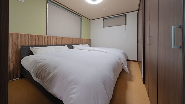 A neatly made bed in a hotel room with a wooden headboard, a small window, and a wardrobe. - Takayama Stay Karatachi DX-B (Takayama)