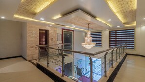 A modern hotel lobby with a marble floor, a glass railing, a chandelier, and a staircase. - Treebo Empire Red Carpet (Agra)