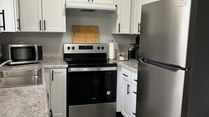A compact kitchen with white cabinets, a stainless steel refrigerator, a microwave, an oven, and a coffee maker.