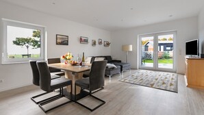 Ein modernes Wohnzimmer mit Essbereich, einer Couch, einem Fernseher und einem großen Fenster mit Blick ins Freie.