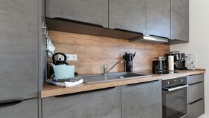 Eine moderne Küche mit grauen Schränken, einer Holz Arbeitsplatte, einer Spüle, einer Kaffeemaschine und einem Backofen.