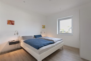 Un dormitorio moderno con cama, mesitas de noche, una ventana y obras de arte en las paredes.