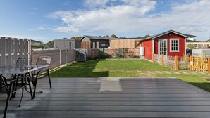 Ein Garten mit einer Holzterrasse, einem roten Gebäude und einem eingezäunten Bereich.