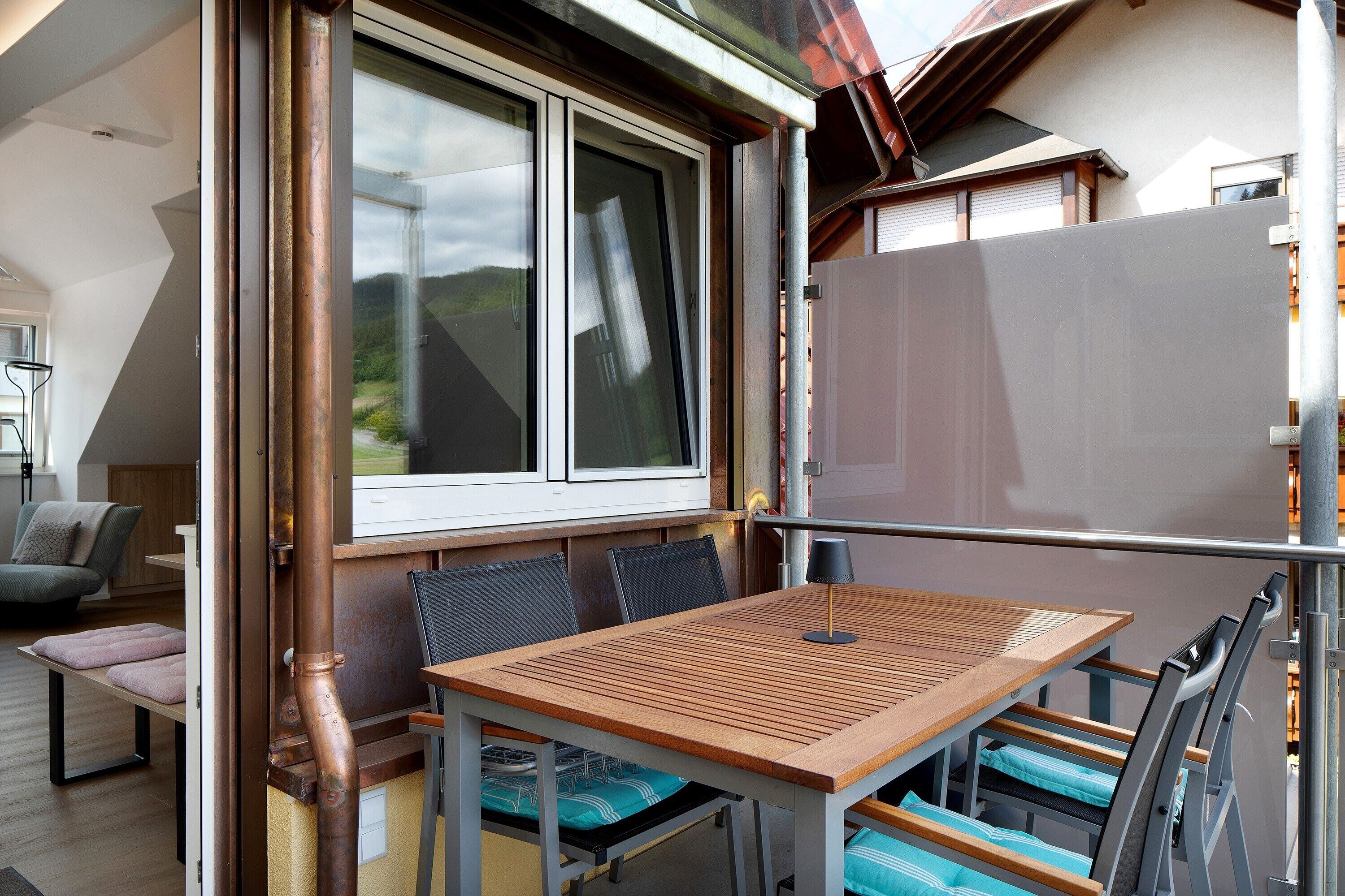 Un coin repas avec une table et des chaises, une fenêtre donnant sur un paysage agréable et une rambarde en métal.