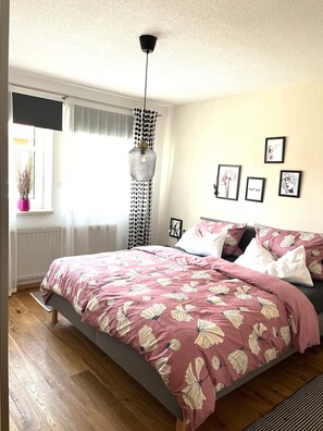 Une chambre à coucher avec un lit, une fenêtre avec des rideaux, un radiateur et des œuvres d’art murales.