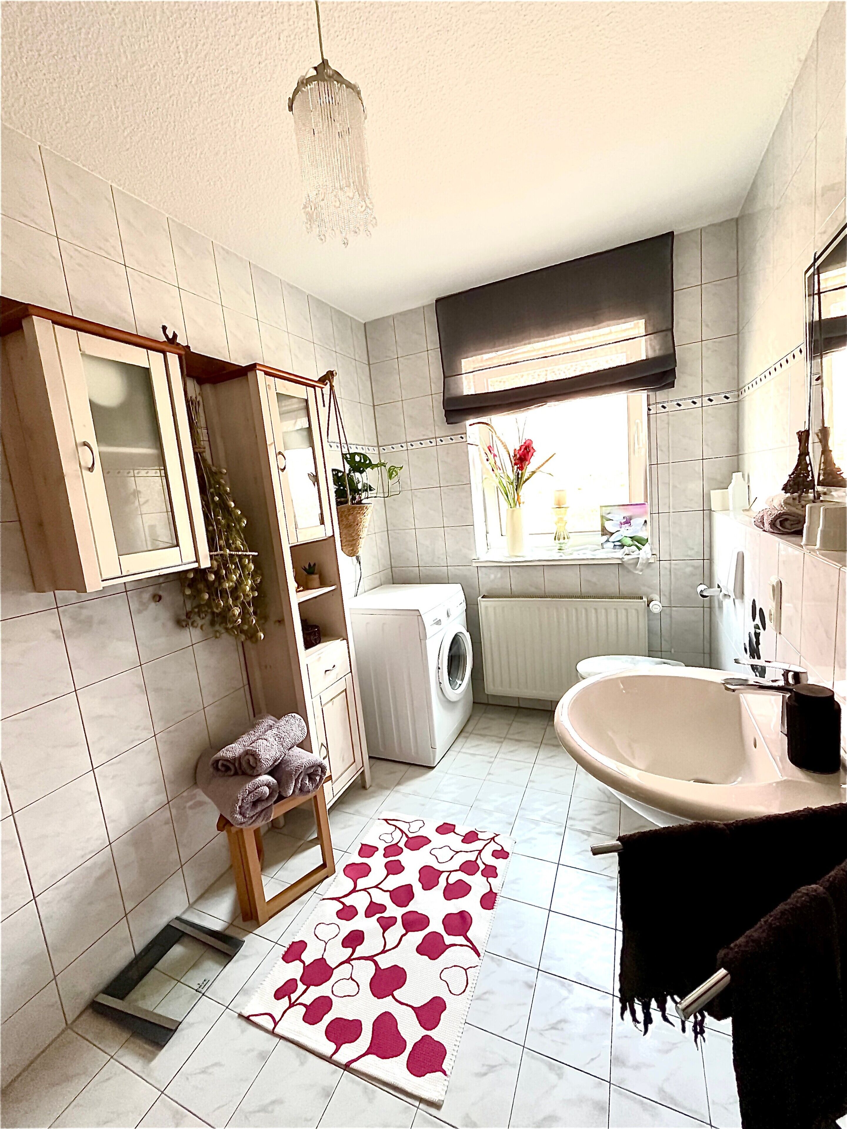 A bathroom with a washing machine, a sink, a mirror, and a window with plants.