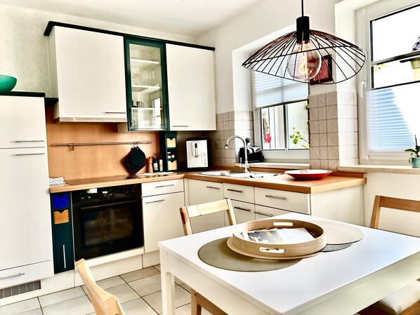 A modern kitchen with white cabinetry, a built-in oven, a sink, and a dining area with a table and chairs.