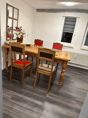 A dining area with a wooden table and chairs, a mirror, and a window with blinds.
