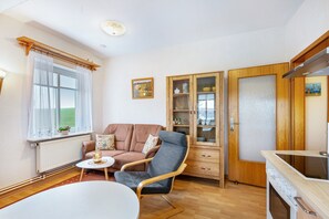 En stue med sofa, stol, lille bord, skab og et køkkenområde med komfur.