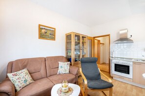 En stue med en brun sofa, en grå lænestol, et lille bord med et lys og et skab med glasdøre.