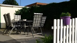 Ein Terrassenbereich im Freien mit Tisch und Stühlen, einem weißen Zaun und einem Blumentopf.