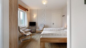 Ein Schlafzimmer mit zwei Betten, einem Fernseher, einem Sessel, einem kleinen Tisch und einem Fenster.