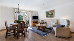 Una sala de estar con una mesa de comedor, sillas, un sofá, un televisor y un cuadro en la pared.