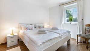 Un dormitorio con una cama grande, mesitas de noche, una silla y una ventana con cortinas.