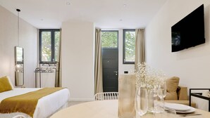 A modern hotel room with a bed, a dining table set for two, a TV mounted on the wall, and large windows with curtains. - Romantic Apartment N5 Oceanografico Virkin Suites (València)