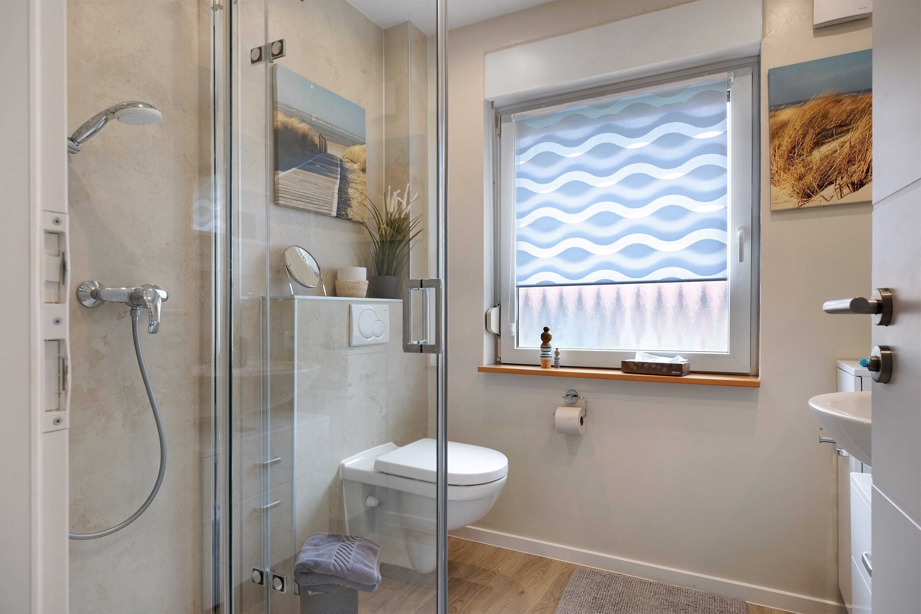Un baño moderno con cabina de ducha de vidrio, inodoro, lavabo y ventana con cortina de estampado ondulado.