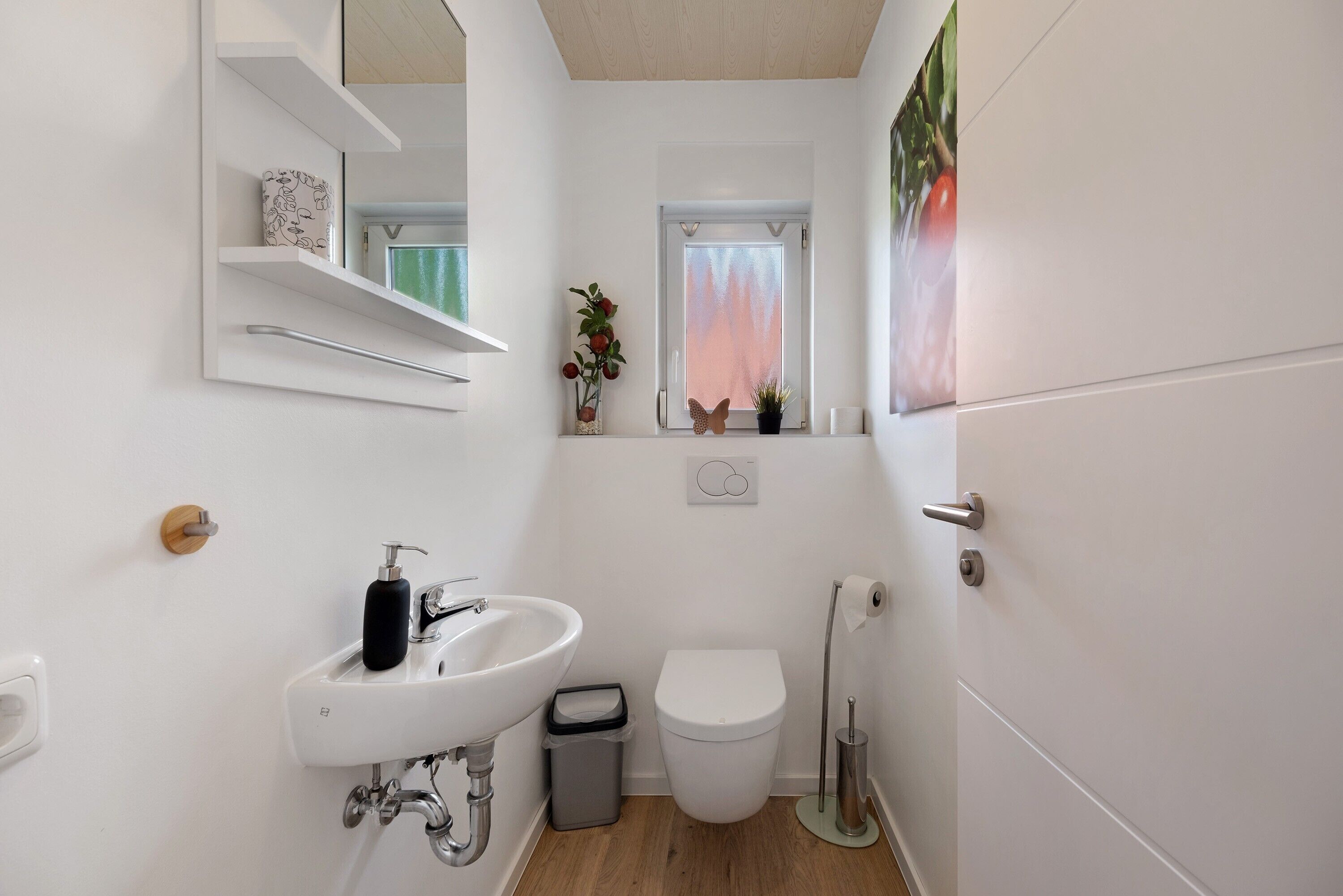 A compact bathroom with a white sink, toilet, and a small window with a view of trees.