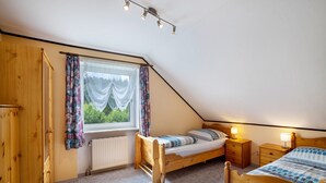 A bedroom with a sloped ceiling, a wooden bed, a window with curtains, a radiator, and a wooden wardrobe. - Apartment 'Ferienwohnung Bächer' with Shared Garden, Balcony and Wi-Fi (Wiesau)