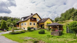 A yellow house with a balcony, a stone wall, and a small wooden structure. - Apartment 'Ferienwohnung Bächer' with Shared Garden, Balcony and Wi-Fi (Wiesau)
