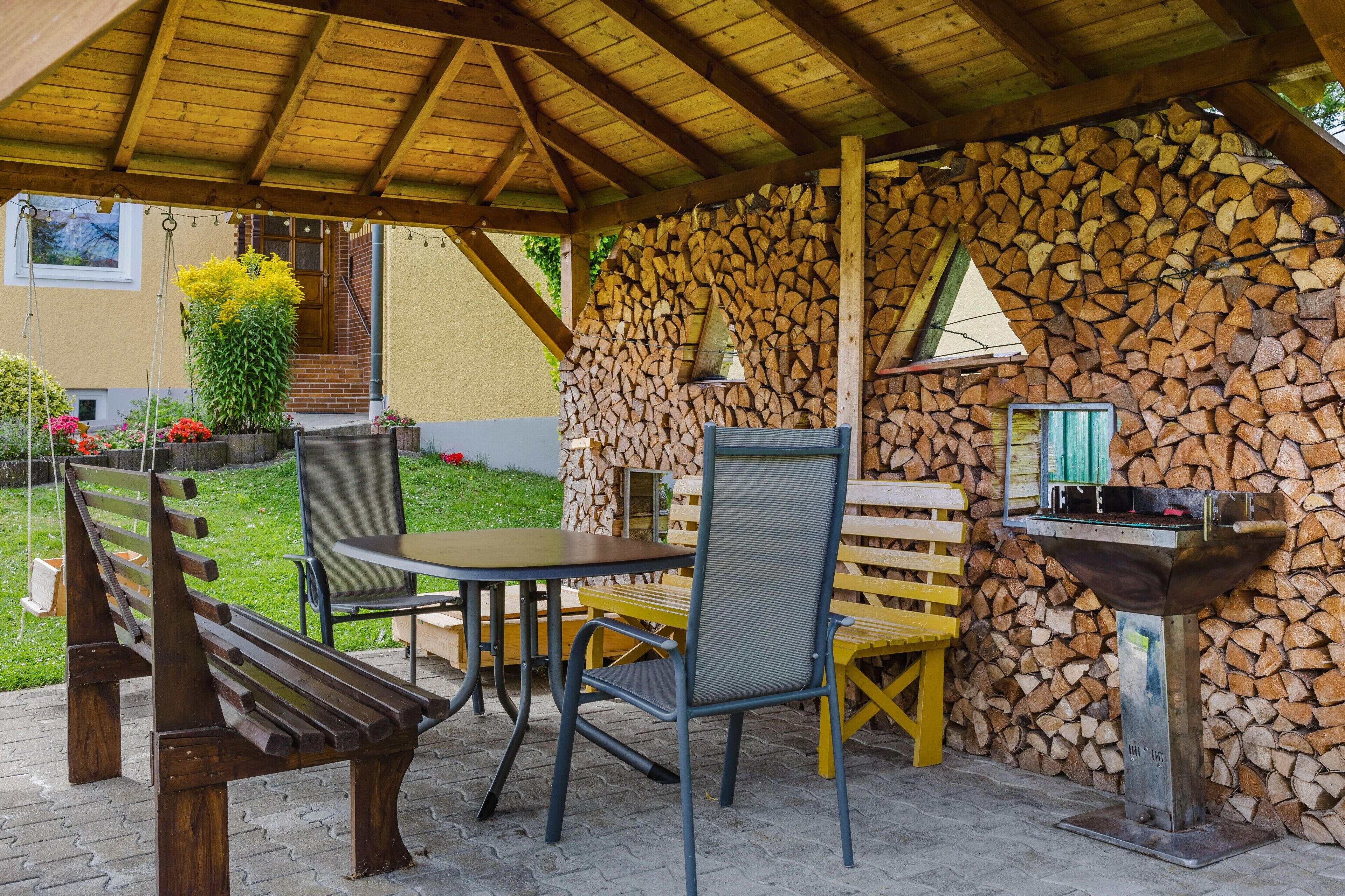 An outdoor patio with a wooden table and chairs, a barbecue grill, and a stone wall.