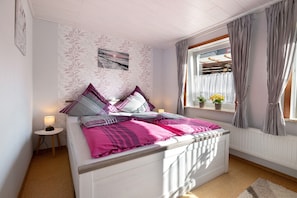 A bedroom with a bed, a nightstand, a window with curtains, and a wall with a leaf pattern.