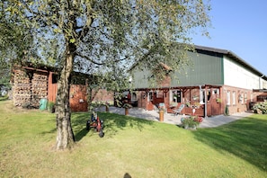 A brick building with a green roof, a covered patio area, and a tree in the foreground.