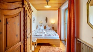 A bedroom with a wooden ceiling, a bed with floral bedding, a wooden wardrobe, and a window with curtains. - Apartment 'Ferienwohnung 3' with Mountain View, Shared Garden and Wi-Fi (Grassau)