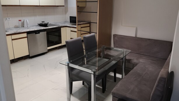 A compact kitchen with a dining area, including a glass table and chairs, a sofa, and built-in appliances. - Apartment in Krumbach with Shared Terrace (Krumbach (Schwaben))