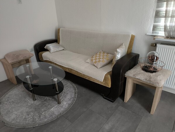 Un salon moderne avec un canapé, une table basse en verre, une table d’appoint et un radiateur.