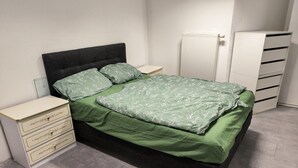 A bed with a green bedspread, a bedside table with drawers, a radiator, and a wardrobe. - Apartment in Krumbach with Shared Terrace (Krumbach (Schwaben))