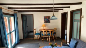 Una habitación con una mesa de comedor, sillas, un sofá, una mesita con un jarrón y un colgador de luz.