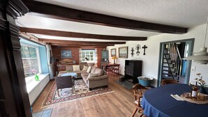A cozy living room with a fireplace, a dining area with a table set for two, and a large window with curtains.