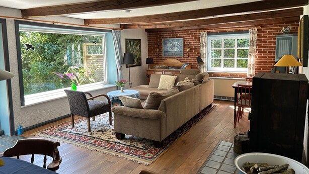 A cozy living room with a sofa, chairs, a fireplace, and large windows.