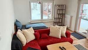 Un salon moderne avec un canapé d’angle rouge, une table basse en bois et une vue sur l’extérieur.