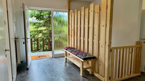 Ein Zimmer mit einer Bank, einer Holzwand und einer Tür, die auf einen Balkon mit Blick ins Grüne führt.
