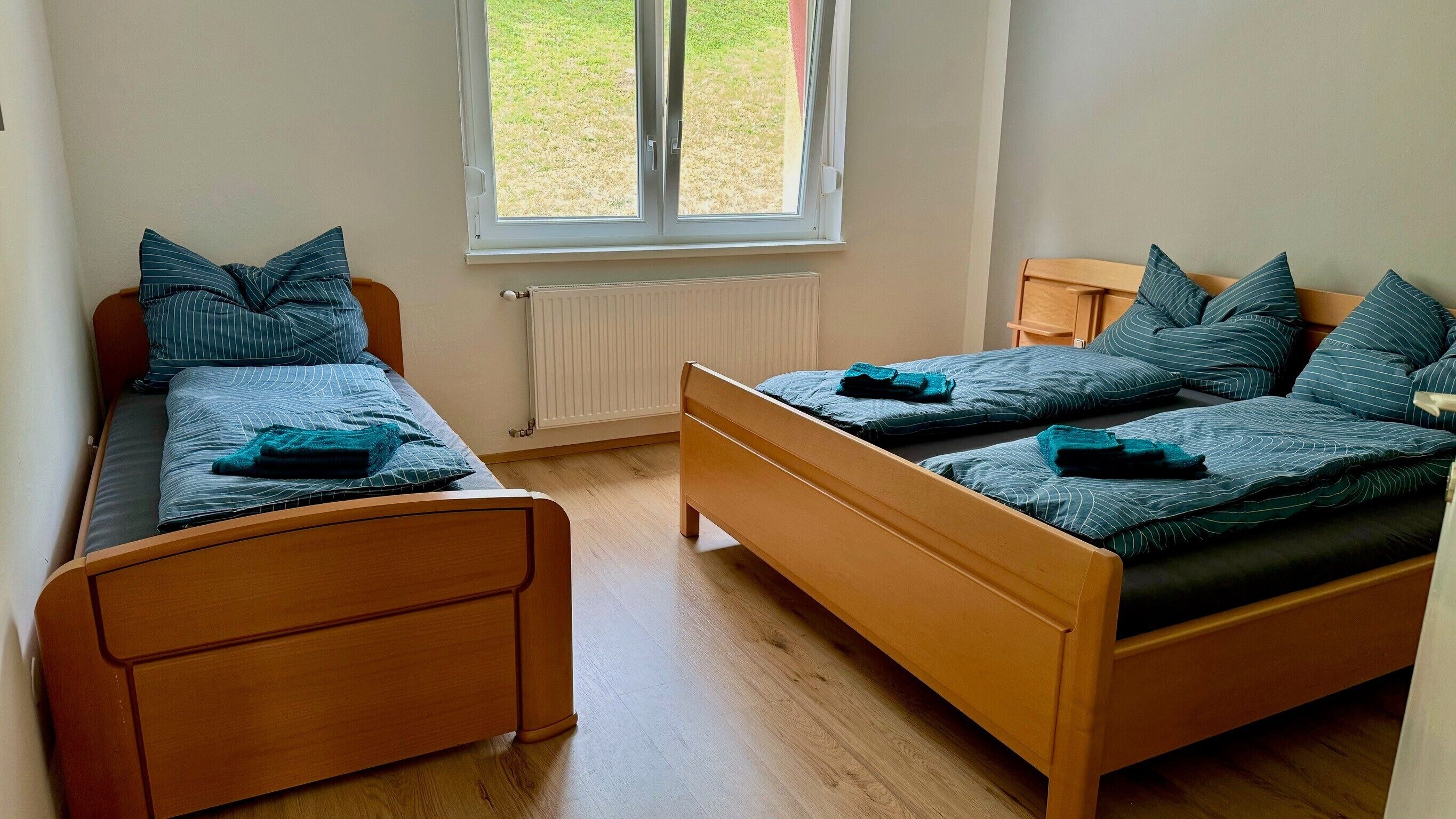 A room with two wooden beds, a window with a view of the outdoors, and a radiator.