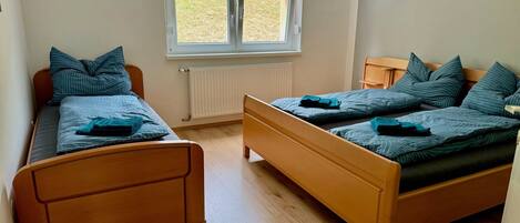 A room with two wooden beds, a window with a view of the outdoors, and a radiator.