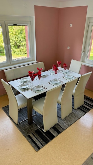 Comedor con mesa preparada para seis personas, sillas blancas y vista a zonas verdes.