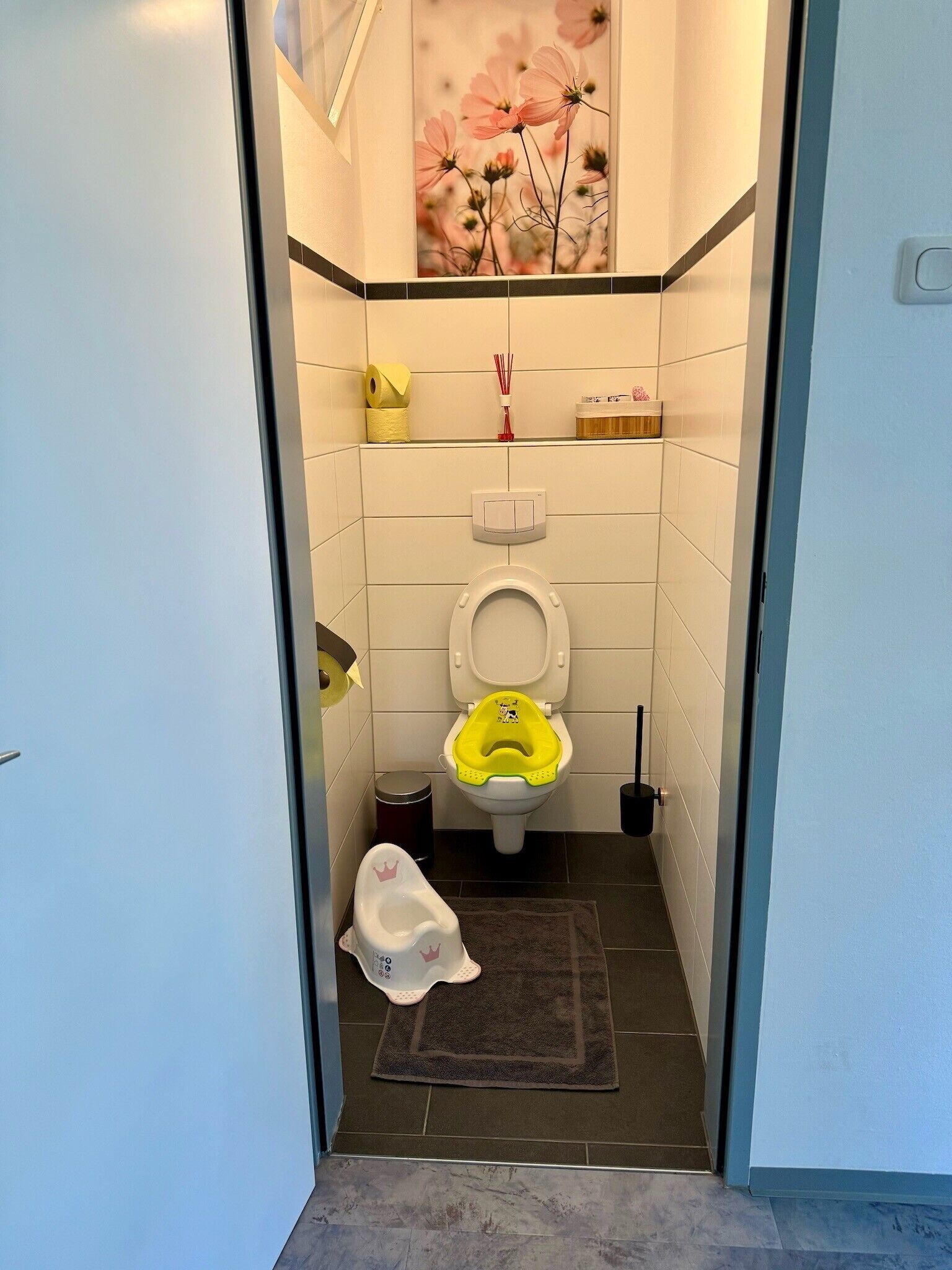 A bathroom with a toilet, a trash bin, a rug, and a painting on the wall.