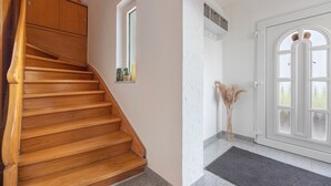 Un escalier en bois menant à un palier, une porte blanche avec des panneaux de verre et une petite fenêtre donnant sur le paysage.