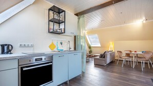 Une cuisine moderne dotée d’un four encastré, un coin repas avec une table et des chaises, et un petit espace détente avec un canapé.