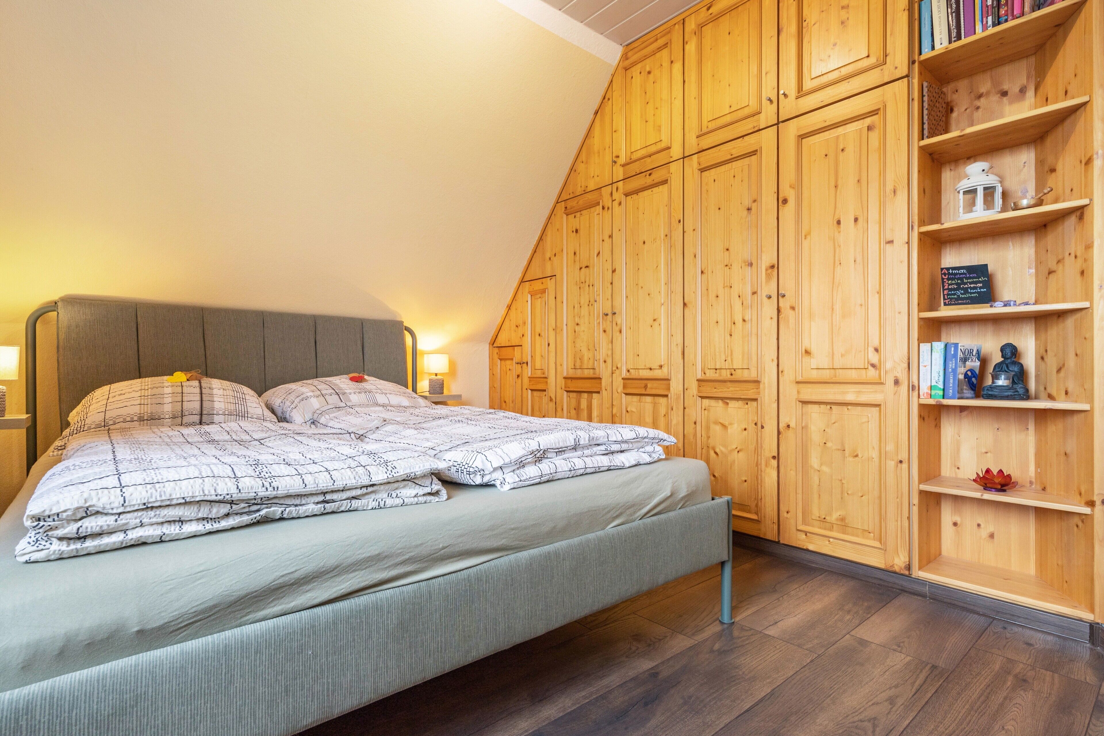 Un dormitorio con cama, armario de madera y estante con libros y objetos decorativos.
