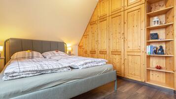 Un dormitorio con cama, armario de madera y estante con libros y objetos decorativos.