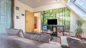 A modern living room with a sofa, a television, a plant, and a bookshelf.