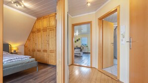 Une chambre à coucher comprenant un lit, une armoire en bois et un couloir menant à un espace de vie.