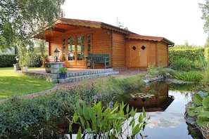 A wooden cabin with a porch, a bench, and a small pond with lily pads. - Apartment 'Offenbüttel' with Private Terrace, Shared Garden and Wi-Fi (Offenbüttel)