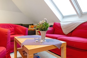 A red couch, a wooden table with a vase and glasses, and a skylight. - Apartment 'Offenbüttel' with Private Terrace, Shared Garden and Wi-Fi (Offenbüttel)