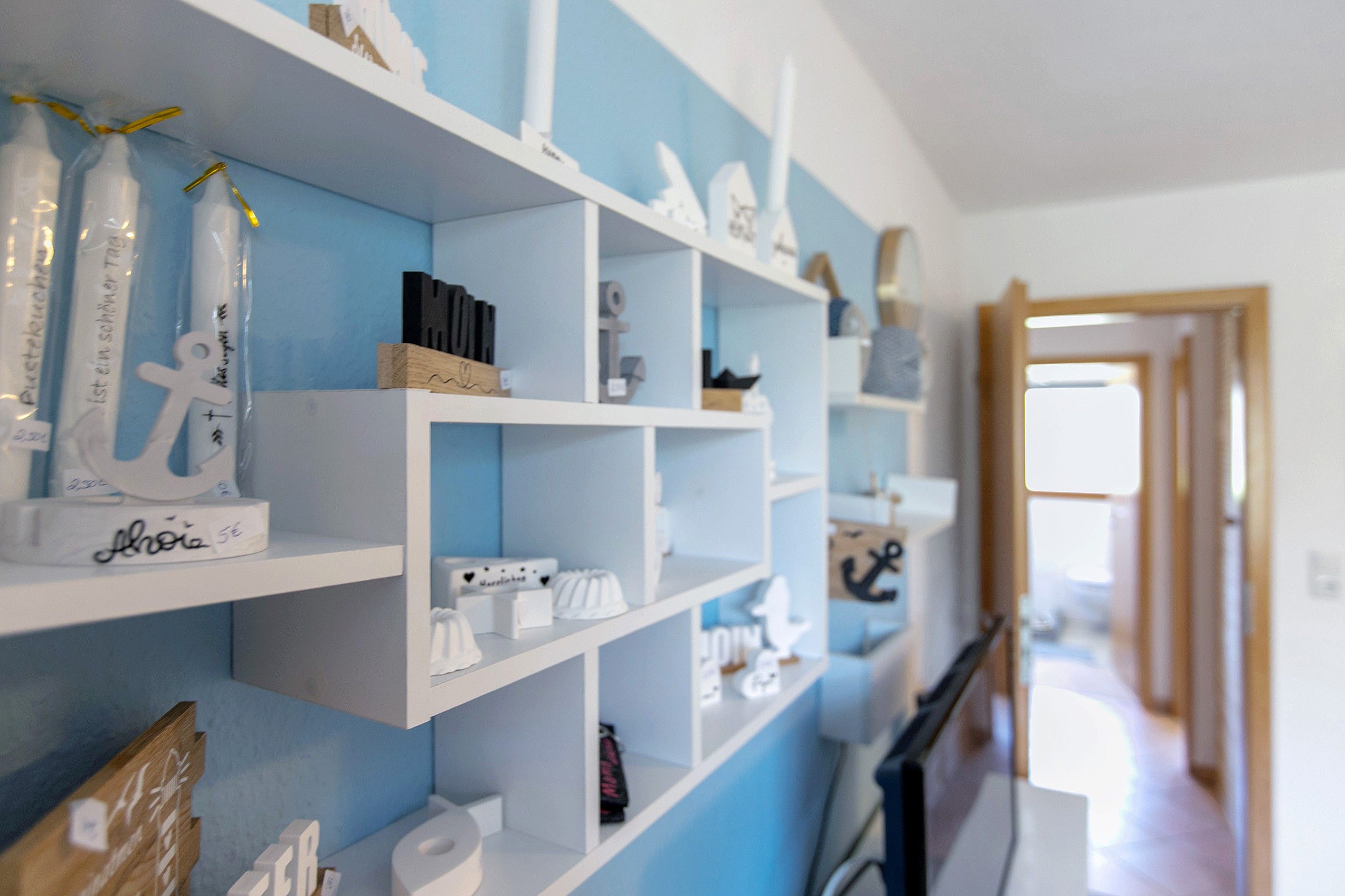 Quarto com estantes brancas contra uma parede azul, exibindo diversos objetos, incluindo uma peça decorativa branca com uma assinatura, um objeto branco com formato de coração e um objeto preto.