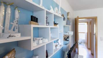 Quarto com estantes brancas contra uma parede azul, exibindo diversos objetos, incluindo uma peça decorativa branca com uma assinatura, um objeto branco com formato de coração e um objeto preto.